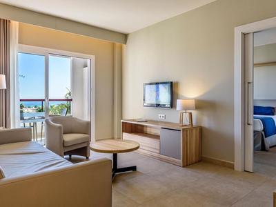 Chambre d'hôtel moderne avec salon, TV, balcon et chambre attenante avec lit double.