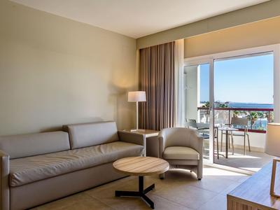 Salon moderne avec canapé, fauteuil et accès au balcon avec vue sur la mer dans une chambre d'hôtel.