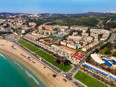 Luftaufnahme eines Strandes mit angrenzender Stadt und Hotels unter klarem Himmel.