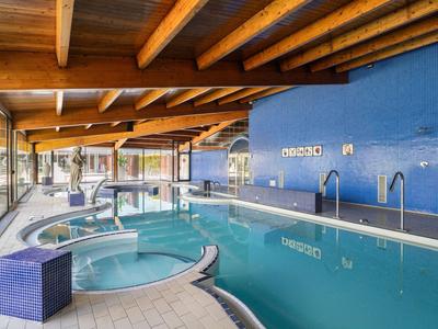 Innenpool mit blauem Wasser, Whirlpool und Holzdecke in einem modernen Hotel.