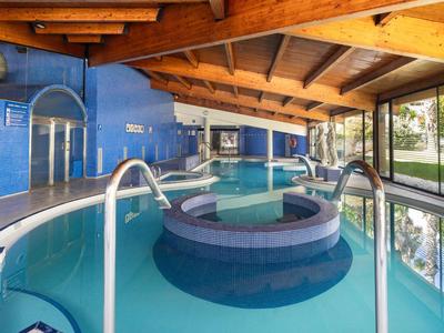 Innenbereich eines Hotels mit großem Whirlpool und Schwimmbad unter Holzdecke und großen Fenstern.