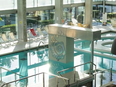 Innenansicht eines modernen Hotels mit einem glänzenden Wasserbecken und großen Glasfenstern.