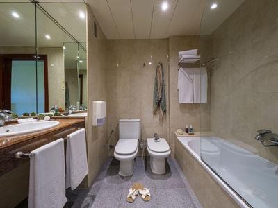 Nowoczesna łazienka z wanną, toaletą, bidetem i dużym lustrem w pokoju hotelowym.