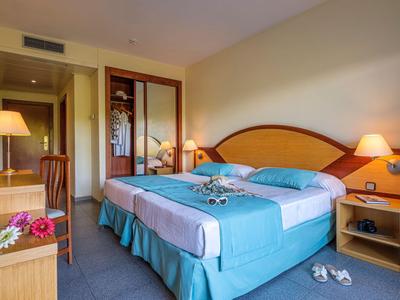 Jasny pokój hotelowy z łóżkiem podwójnym, biurkiem, lustrem i dwoma szafkami nocnymi z lampami.