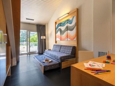 Jasny pokój hotelowy z balkonem, rozkładaną sofą i biurkiem z przyborami do rysowania.