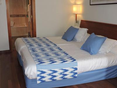 Nowoczesny pokój hotelowy z łóżkiem podwójnym, niebieskim narzutem i widokiem na łazienkę.