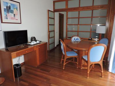 Pokój hotelowy z drewnianą podłogą, okrągłym stołem, niebieskimi krzesłami i biurkiem z telewizorem.