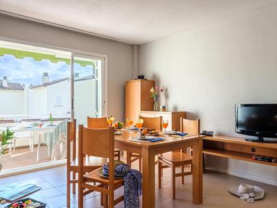 Helles Esszimmer mit Holzmöbeln, Fernseher und Zugang zu einer sonnigen Terrasse.