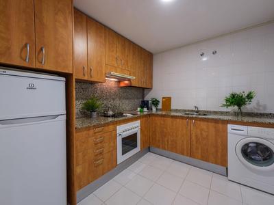 Moderne Küche mit Holzschränken, Kühlschrank, Waschmaschine und hellen Fliesen im Hotelzimmer.