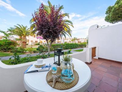 Terrasse mit weißem Tisch, Glasflasche und Tasse vor grünem Garten und blauem Himmel.