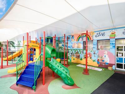 Bunter Kinderspielplatz mit Rutschen und Kletternetzen neben einem Gebäude mit Wandmalereien.