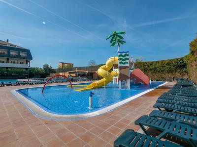 Außenpool mit Wasserrutschen und Liegestühlen vor einem Hotelgebäude bei sonnigem Wetter.
