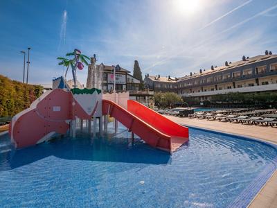 Sommerliches Schwimmbecken mit Kinderrutsche und Liegestühlen im Hotelbereich bei Sonnenschein.