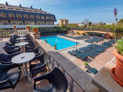 Hotelterrasse mit Pool, schwarzen Stühlen, Tischen und Sonnenschirmen bei klarem Himmel.