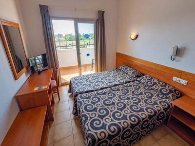 Kleines Hotelzimmer mit zwei Einzelbetten, Balkon und Schreibtisch mit Spiegel und Fernseher.