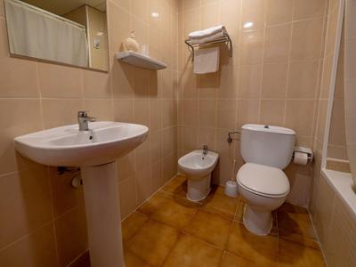 Kleines Badezimmer mit Waschbecken, Bidet, Toilette, Handtüchern und braunen Fliesen.