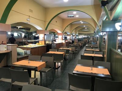 Innenraum eines modernen Restaurants mit Reihen von Holz- und schwarzem Mobiliar unter gewölbten Decken.
