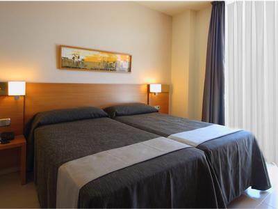 Ein Doppelbett mit grauen Bettdecken in einem hellen, modern eingerichteten Hotelzimmer.