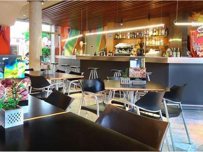 Moderner Hotelbarbereich mit dunklen und hellen Stühlen, Tischen und einer gut beleuchteten Theke.