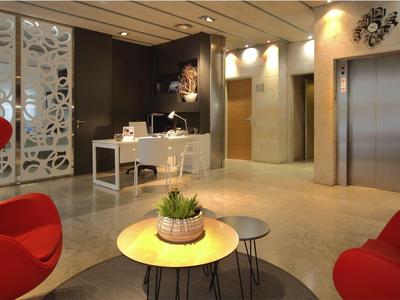 Moderner Hotel-Lobby mit Rezeption, roten Sesseln und Aufzügen im Hintergrund.