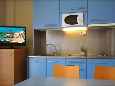 Küchenzeile mit blauen Schränken, Mikrowelle, kleinem Fernsehgerät und orangenen Stühlen.