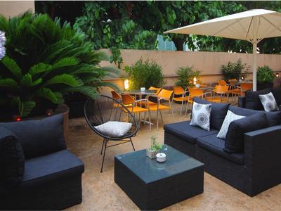 Moderne Terrasse mit schwarzen Sitzmöbeln, Kissen, Pflanzen und Sonnenschirm im Hotelaußenbereich.