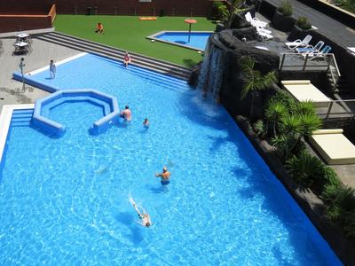 Großer Pool mit Wasserfall, Sonnenterrasse und Menschen, die im Wasser entspannen.