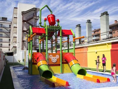 Bunter Wasserspielplatz mit Rutschen und Wasserkanonen vor Hochhäusern unter blauem Himmel.