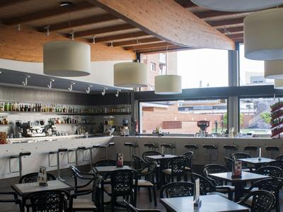 Modernes Hotelrestaurant mit Bar, Tischen und Stühlen, beleuchtet durch große Fenster.
