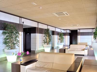 Heller Hotel-Loungebereich mit bequemen Sofas, großen Pflanzen und moderner Decke.