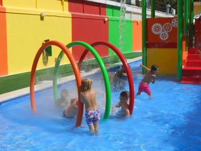 Kinder spielen in einem farbenfrohen Wasserspielbereich mit bunten Bögen und spritzendem Wasser.