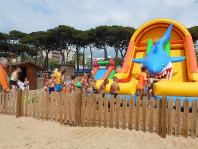 Kinder spielen auf einem aufblasbaren Wasserspielplatz am Strand neben einem Holzzaun.
