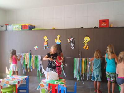 Kinder spielen in einem bunten Raum mit einer Tischdecke und Girlanden an der Wand.