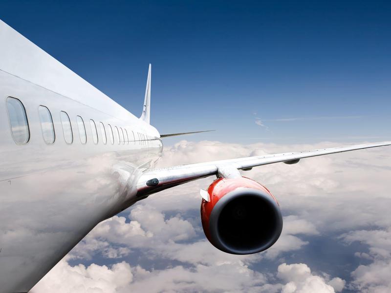 Flugzeugflügel mit Triebwerk in der Luft, blauer Himmel und weiße Wolken darunter.