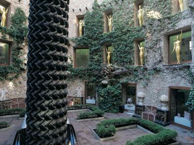 Innenhof mit begrünten Wänden, großen Fenstern und einem skulpturalen Säulenelement im Zentrum.