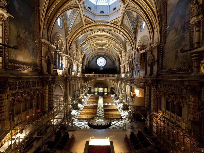 Prächtiger Kirchensaal mit hohen Bögen, gemalten Wänden und leuchtenden Kerzen.
