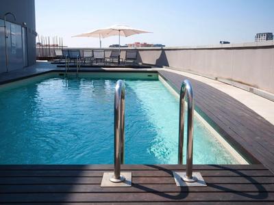 Piscine d'hôtel moderne avec terrasse en bois et parasols sur le toit par ciel clair.