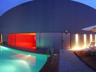 Nowoczesny basen wieczorem z oświetlonym basenem i strefą wypoczynkową.