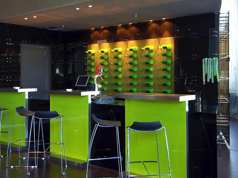 Nowoczesny bar hotelowy z zielonymi akcentami, wysokimi hokerami i stonowanym oświetleniem.