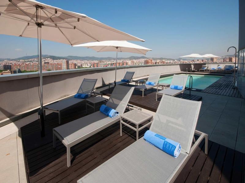 Taras na dachu z leżakami, parasolami i basenem z widokiem na miasto w pogodny dzień.