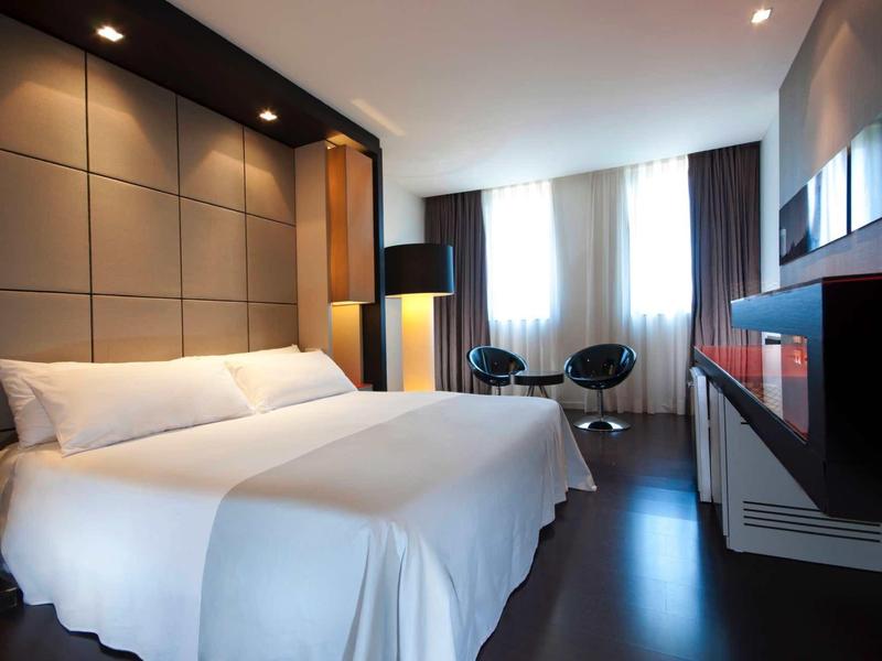 Nowoczesny pokój hotelowy z dużym łóżkiem, częścią wypoczynkową i telewizorem na ścianie.