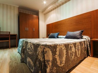 Una habitación de hotel sencilla con cama doble, muebles de madera y colcha estampada.