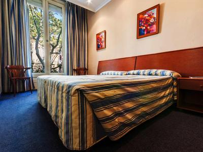 Habitación de hotel con cama doble, alfombra azul oscuro y dos cuadros en la pared.