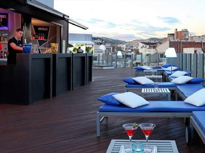 Střešní terasa s modrými polstrovanými lehátky a barem, výhled na město a hory.