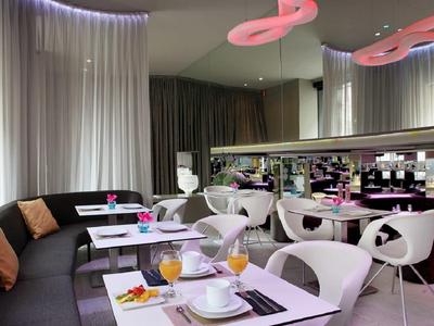 Moderní hotelová restaurace s bílým nábytkem, pohovkami a dekorativním osvětlením.