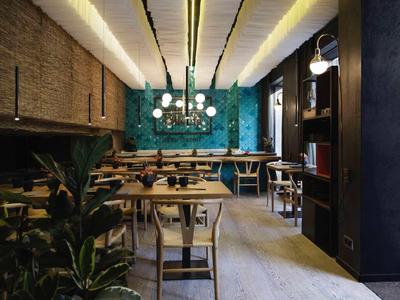 Moderní restaurace s dřevěnými stoly, zelenou zdí a dekorativním osvětlením.