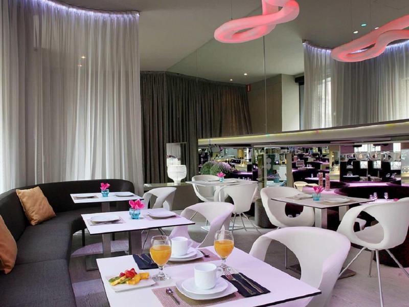 Modernes, gemütliches Café mit geschwungener schwarzer Sitzbank, weißen Stühlen und rosa Akzenten.