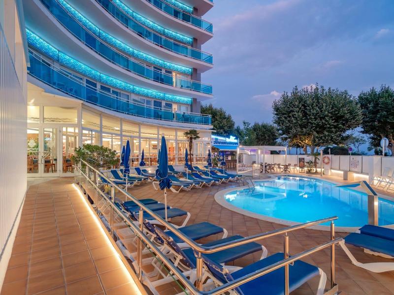 Vue du soir d'un hôtel avec piscine éclairée et chaises longues sur la terrasse.