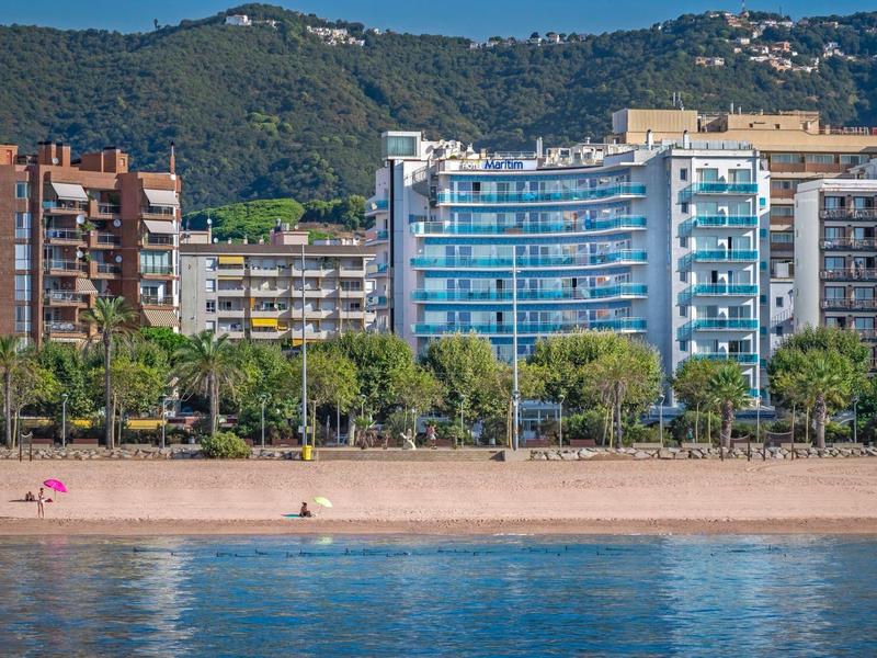 Plage avec quelques personnes et hôtels devant des collines boisées en arrière-plan