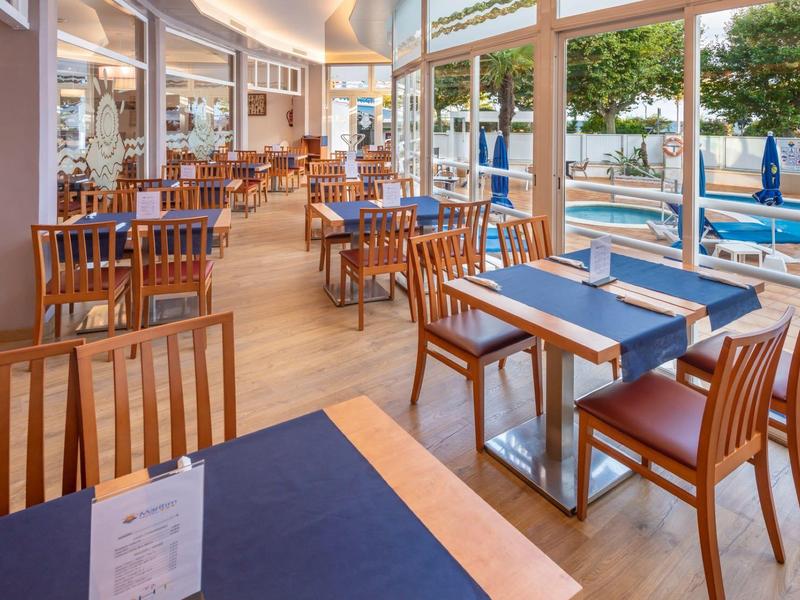 Restaurant lumineux avec chaises et tables en bois, nappes bleues, vue sur une piscine.